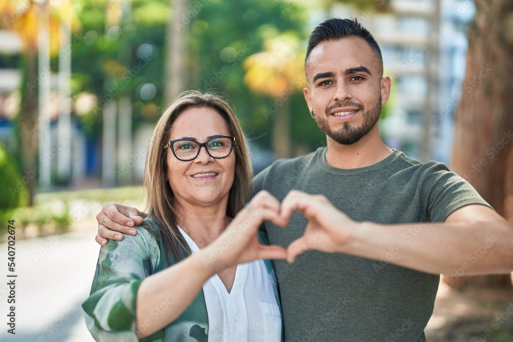 Naklejka premium Man and woman mother and daugther doing heart gesture with hands at park
