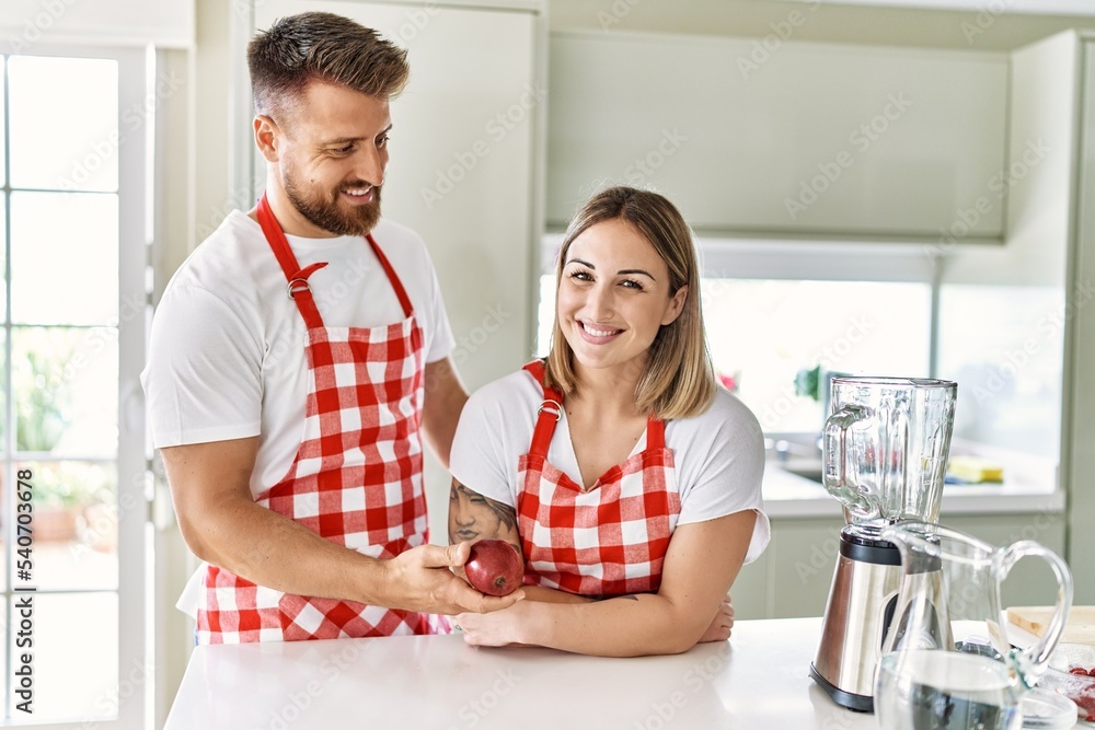 Obraz premium Young couple smiling confident holding red apple at kitchen