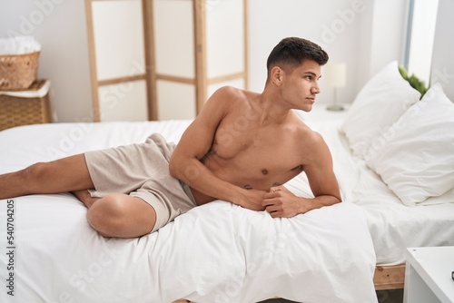 Young hispanic man lying on bed with relaxed expression at bedroom