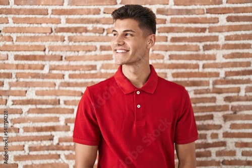 Young hispanic man standing over bricks wall smiling looking to the side and staring away thinking.