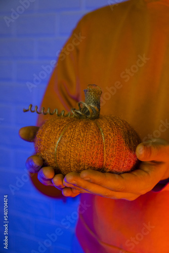 Knitted pumpkin in the hands of a man on Halloween on a colored background. Home decoration. Warm home decor. Halloween scary background. Halloween party. Halloween celebration.