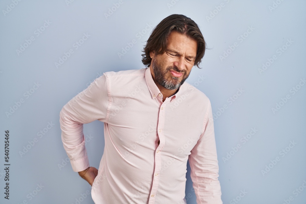 Handsome middle age man wearing elegant shirt background suffering of backache, touching back with hand, muscular pain Handsome middle age man wearing elegant shirt background suffering of backache, touching back with hand, muscular pain