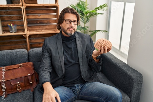 Fotografie Handsome middle age man at consultation office holding brain thinking attitude a