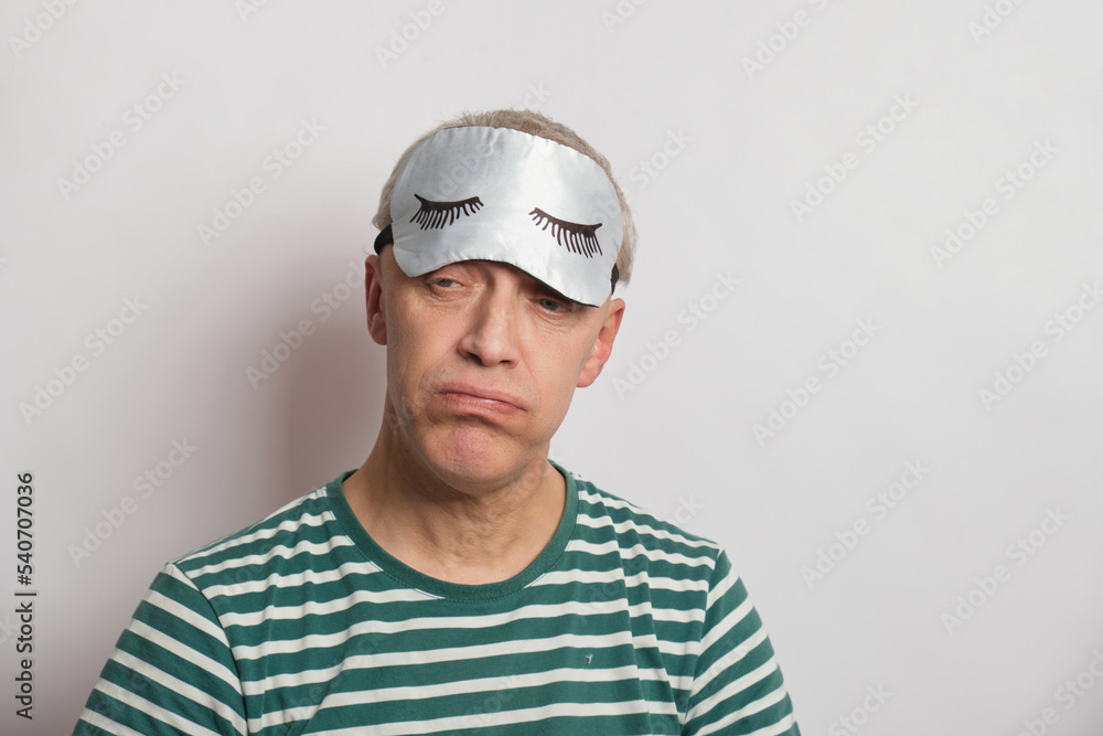 tired man in a sleep mask on a gray background, insomnia of the elderly concept, sleep problems tired man in a sleep mask on a gray background, insomnia of the elderly concept, sleep problems