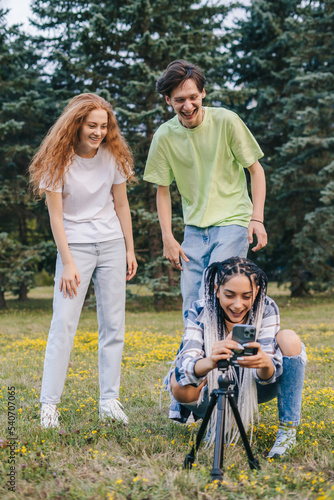 Young three influencers fixing the phone tripod for making a selfie on for their followers. Popularity in internet, friendship. Making content for social media