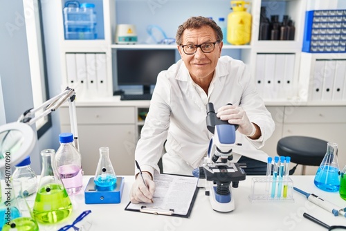 Middle age man wearing scientist uniform using microscope at laboratory