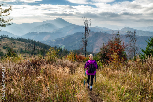 Woman with trkking poles hiking in autumn mountains photo