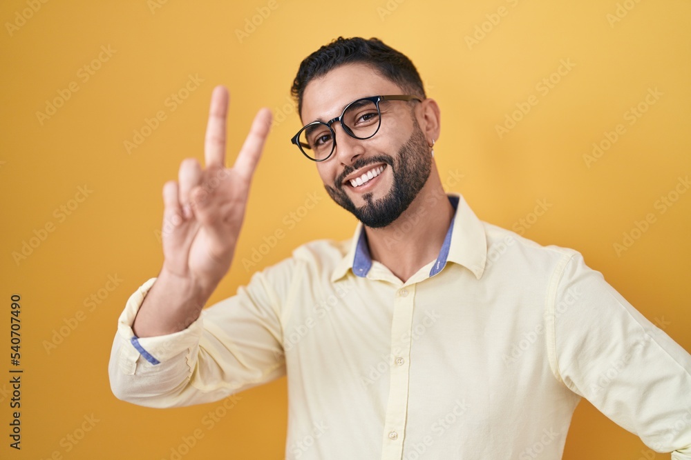 Hispanic young man wearing business clothes and glasses smiling looking to the camera showing fingers doing victory sign. number two. Hispanic young man wearing business clothes and glasses smiling looking to the camera showing fingers doing victory sign. number two.