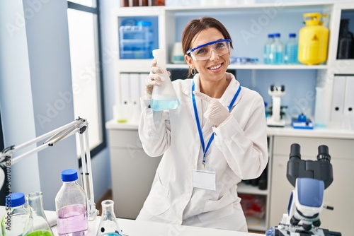 Young brunette woman working at scientist laboratory smiling happy pointing with hand and finger