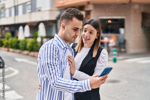 Man and woman couple hugging each other using smartphone at street