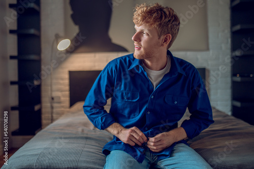 A young man in dark-blue shirt sitting on the bed