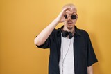 Young caucasian man wearing sunglasses standing over yellow background doing ok gesture shocked with surprised face, eye looking through fingers. unbelieving expression.