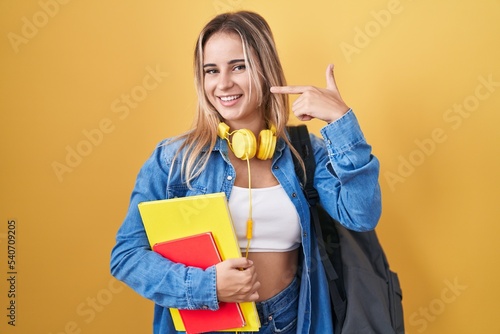 Young blonde woman wearing student backpack and holding books smiling cheerful showing and pointing with fingers teeth and mouth. dental health concept.