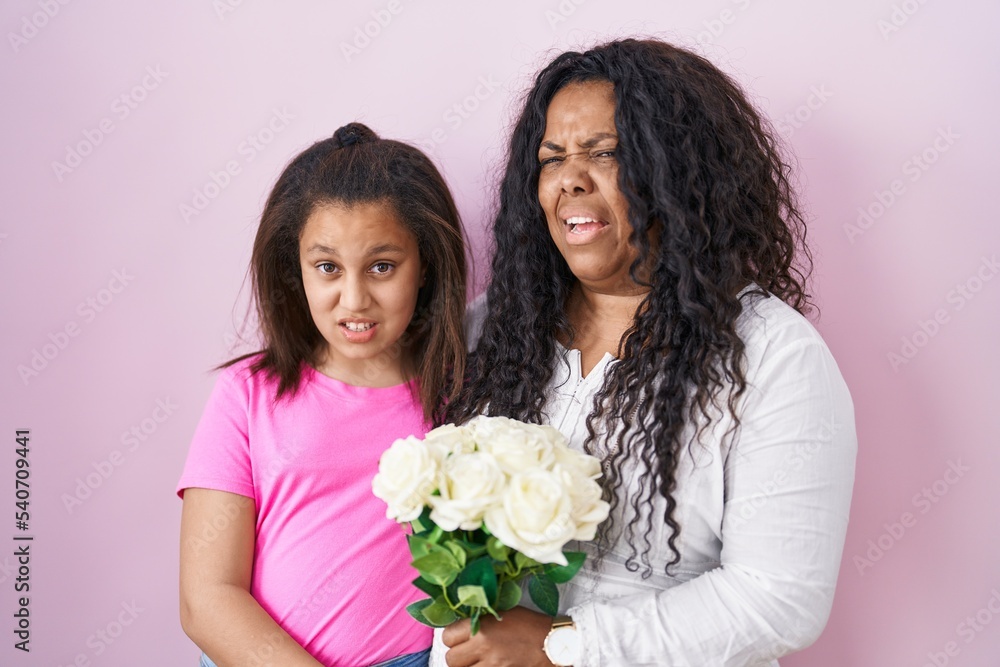 Mother and young daughter holding bouquet of white flowers clueless and confused expression. doubt concept. Mother and young daughter holding bouquet of white flowers clueless and confused expression. doubt concept.