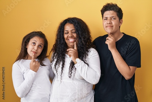 Family of mother, daughter and son standing over yellow background thinking concentrated about doubt with finger on chin and looking up wondering