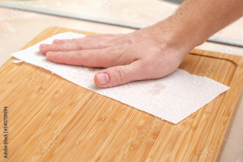A man wipes a bamboo cutting board with a white paper napkin after washing with water. Careful handling of wood products. Bamboo cutting board. Treatment with mineral oil. Drying of the cutting board.
