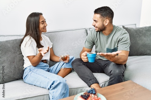 Young latin couple having breakfast sitting on the sofa at home.