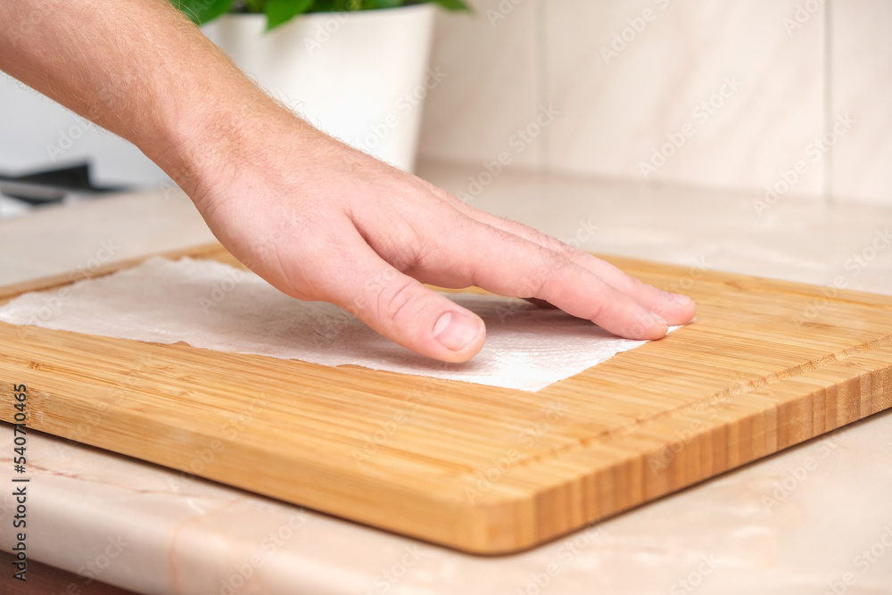 A man wipes a bamboo cutting board with a white paper napkin after washing with water. Careful handling of wood products. Bamboo cutting board. Treatment with mineral oil. Drying of the cutting board. A man wipes a bamboo cutting board with a white paper napkin after washing with water. Careful handling of wood products. Bamboo cutting board. Treatment with mineral oil. Drying of the cutting board.