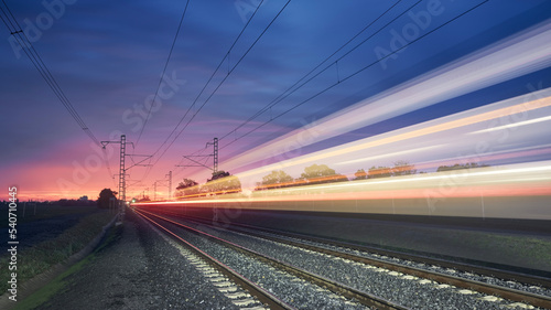 Modern railway at beautiful sunrise. Light trail of high speed train on railroad track. Moving modern intercity passenger train..