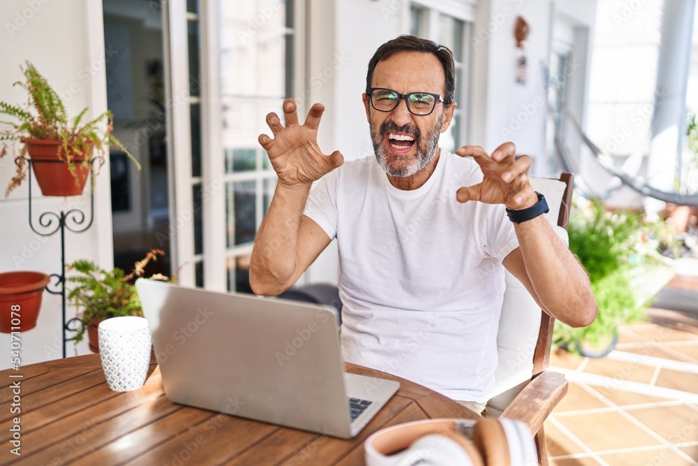 Middle age man using computer laptop at home smiling funny doing claw gesture as cat, aggressive and sexy expression Middle age man using computer laptop at home smiling funny doing claw gesture as cat, aggressive and sexy expression