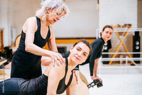 Mature female pilates instructor assisting student on high-low chair during class in exercise studio.