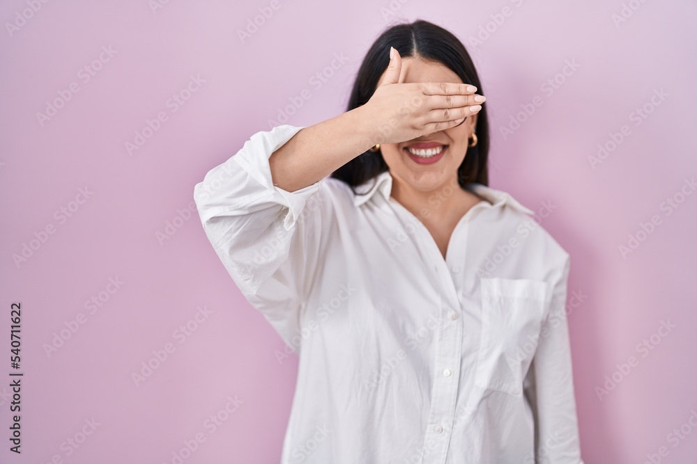 Young brunette woman standing over pink background smiling and laughing with hand on face covering eyes for surprise. blind concept. Young brunette woman standing over pink background smiling and laughing with hand on face covering eyes for surprise. blind concept.