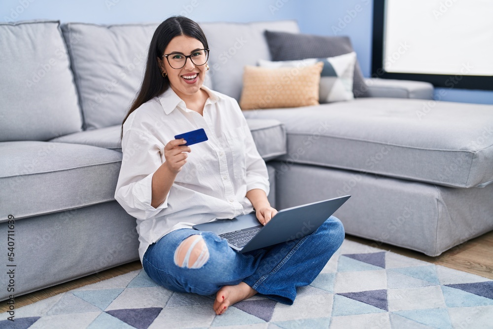 Young hispanic woman using laptop and credit card sitting on sofa at home Young hispanic woman using laptop and credit card sitting on sofa at home