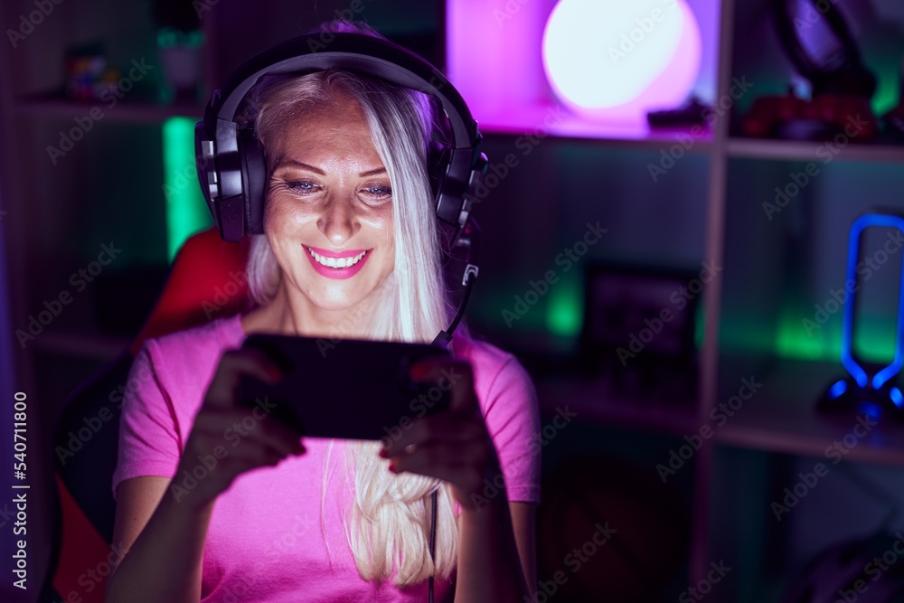 Young blonde woman streamer playing video game by smartphone at gaming room Young blonde woman streamer playing video game by smartphone at gaming room