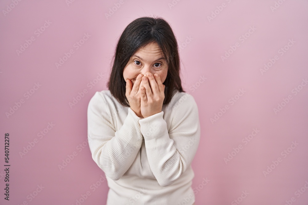 Woman with down syndrome standing over pink background laughing and embarrassed giggle covering mouth with hands, gossip and scandal concept Woman with down syndrome standing over pink background laughing and embarrassed giggle covering mouth with hands, gossip and scandal concept