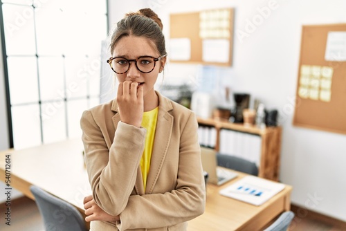 Young brunette teenager wearing business style at office looking stressed and nervous with hands on mouth biting nails. anxiety problem.