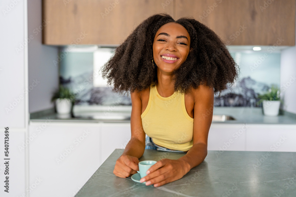 Happy Afro woman with coffee cup in kitchen