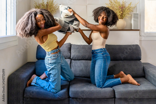 Cheerful multiracial lesbian couple doing pillow fight on sofa photo