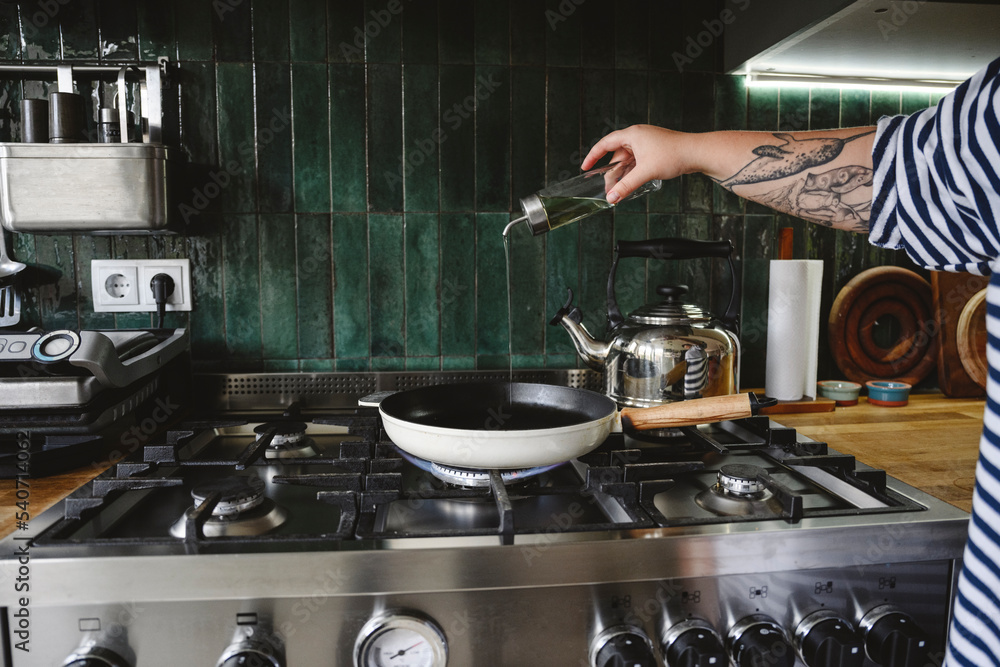 Hand of woman pouring oil in frying pan at home Hand of woman pouring oil in frying pan at home