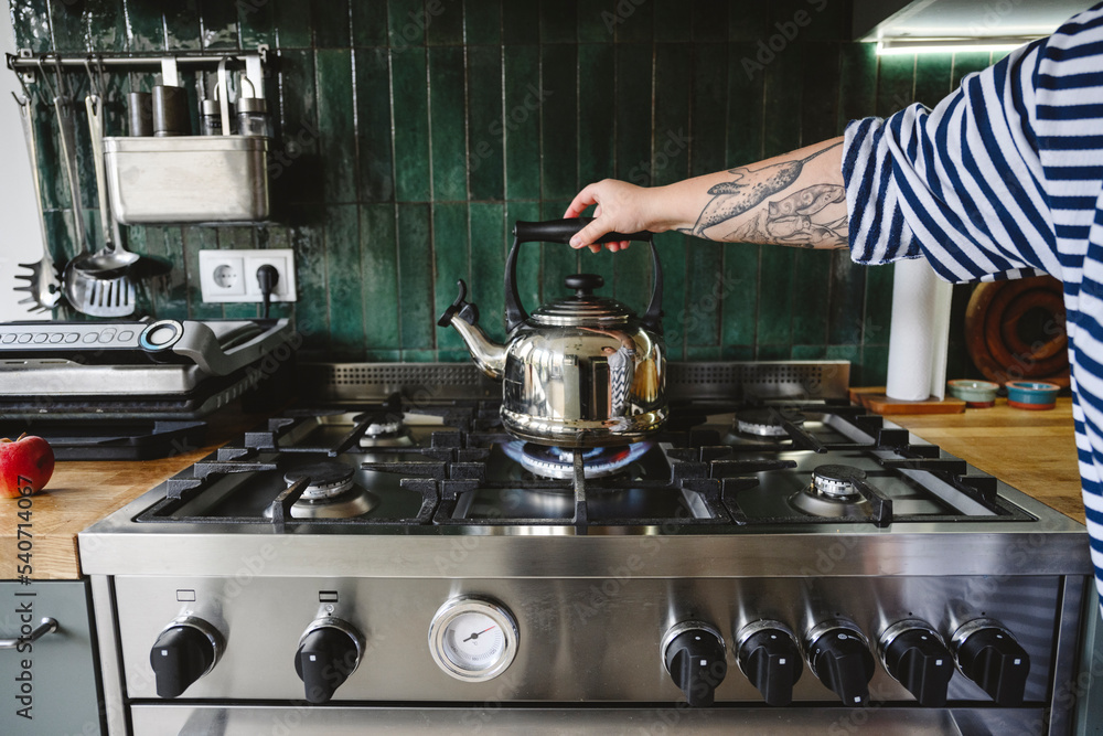 Hand of woman holding kettle on gas stove Hand of woman holding kettle on gas stove