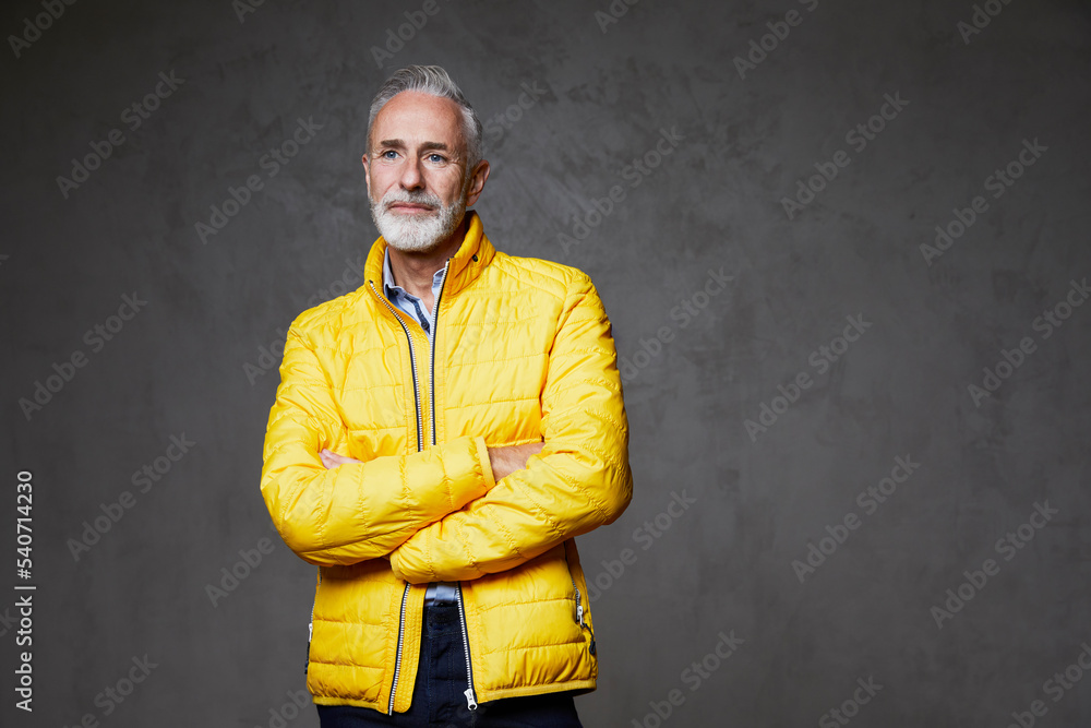 Thoughtful mature man with arms crossed standing in front of grey background Thoughtful mature man with arms crossed standing in front of grey background