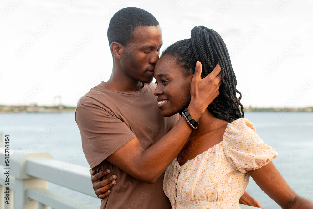 Young man kissing girlfriend by river at sunset Young man kissing girlfriend by river at sunset