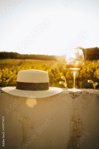 Hat and glass of white wine on wall at sunset photo