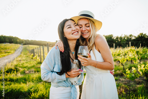 Happy friends holding glass of wine embracing at winery photo