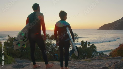 Family surfing. Father and son surfers stand on the coast and watch surfing spot on sunrise