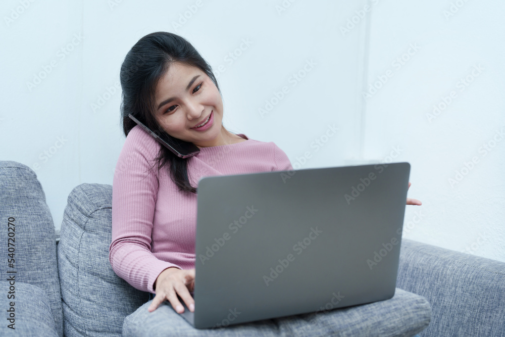 Portrait of a beautiful Asian teenage girl using her phone and computer for video conferencing sitting on the sofa at home Portrait of a beautiful Asian teenage girl using her phone and computer for video conferencing sitting on the sofa at home