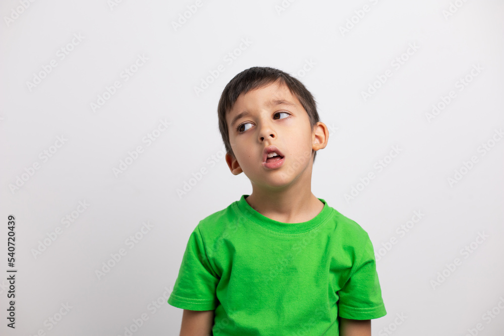 tired boy child in a green T-shirt is having fun on a white background in the studio without baby teeth. tired boy child in a green T-shirt is having fun on a white background in the studio without baby teeth.