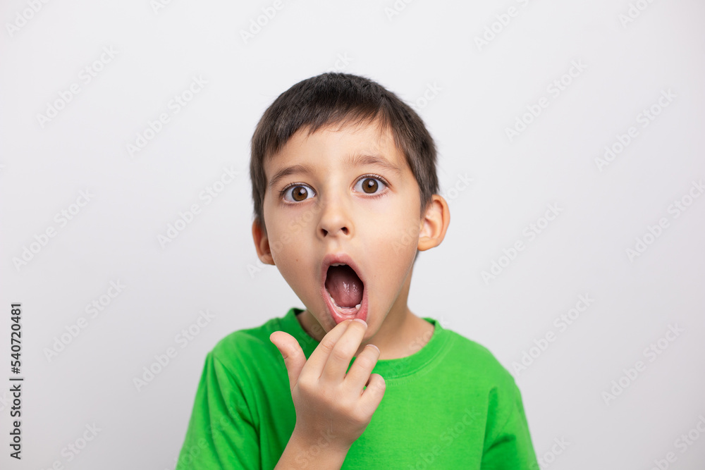 boy child in a green T-shirt is having fun on a white background in the studio without baby teeth. boy child in a green T-shirt is having fun on a white background in the studio without baby teeth.