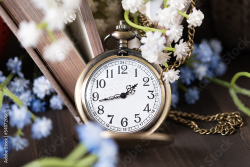 Retro watch on a chain of bronze color among the books and flowers.