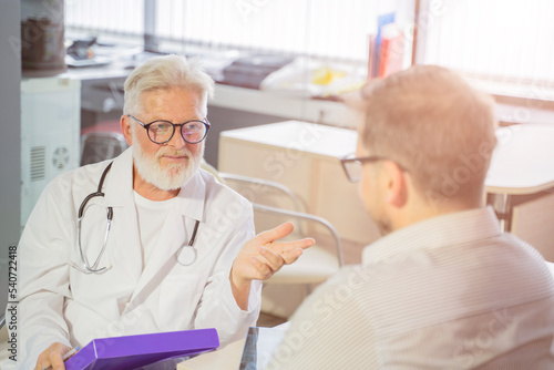 an elderly gray-haired male doctor in a medical office consults a male patient