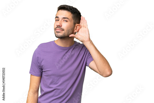 Young handsome caucasian man over isolated background listening to something by putting hand on the ear