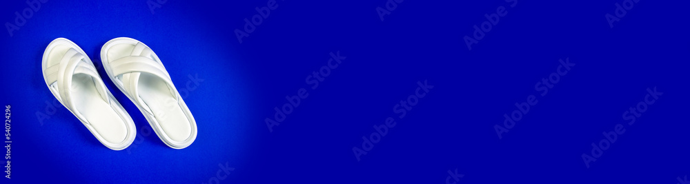 Women's summer white slippers on a blue background. Slippers. Banner for insertion into site. Place for text cope space. Women's summer white slippers on a blue background. Slippers. Banner for insertion into site. Place for text cope space.