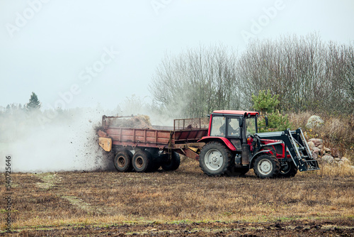 Tractor use manure much spreader trailer to scatter hot steaming horse manure on agriculture field in autumn for natural fertilizer.