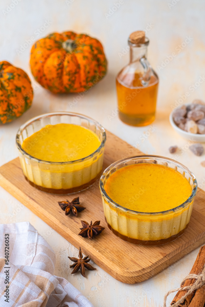 Pumpkin flan, a cold baked dessert of pumpkin puree, eggs, cream and sugar in glass ramekins on a wooden board on a light concrete background. Thanksgiving Day, Halloween Pumpkin flan, a cold baked dessert of pumpkin puree, eggs, cream and sugar in glass ramekins on a wooden board on a light concrete background. Thanksgiving Day, Halloween