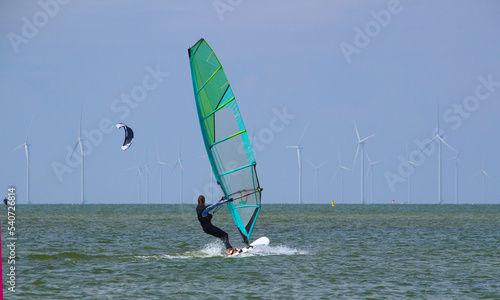 Young woman windsurfing at Ijsselmeer with wind turbines at the horizon (Workum, Netherlands)