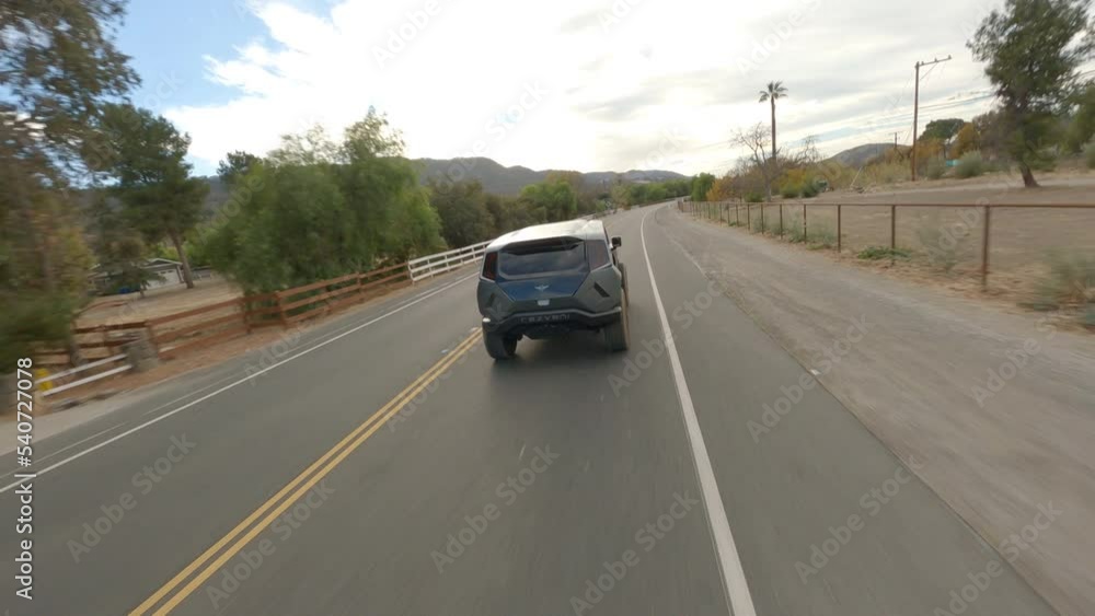 FPV drone chasing shot of new futuristic police car traveling along the road FPV drone chasing shot of new futuristic police car traveling along the road